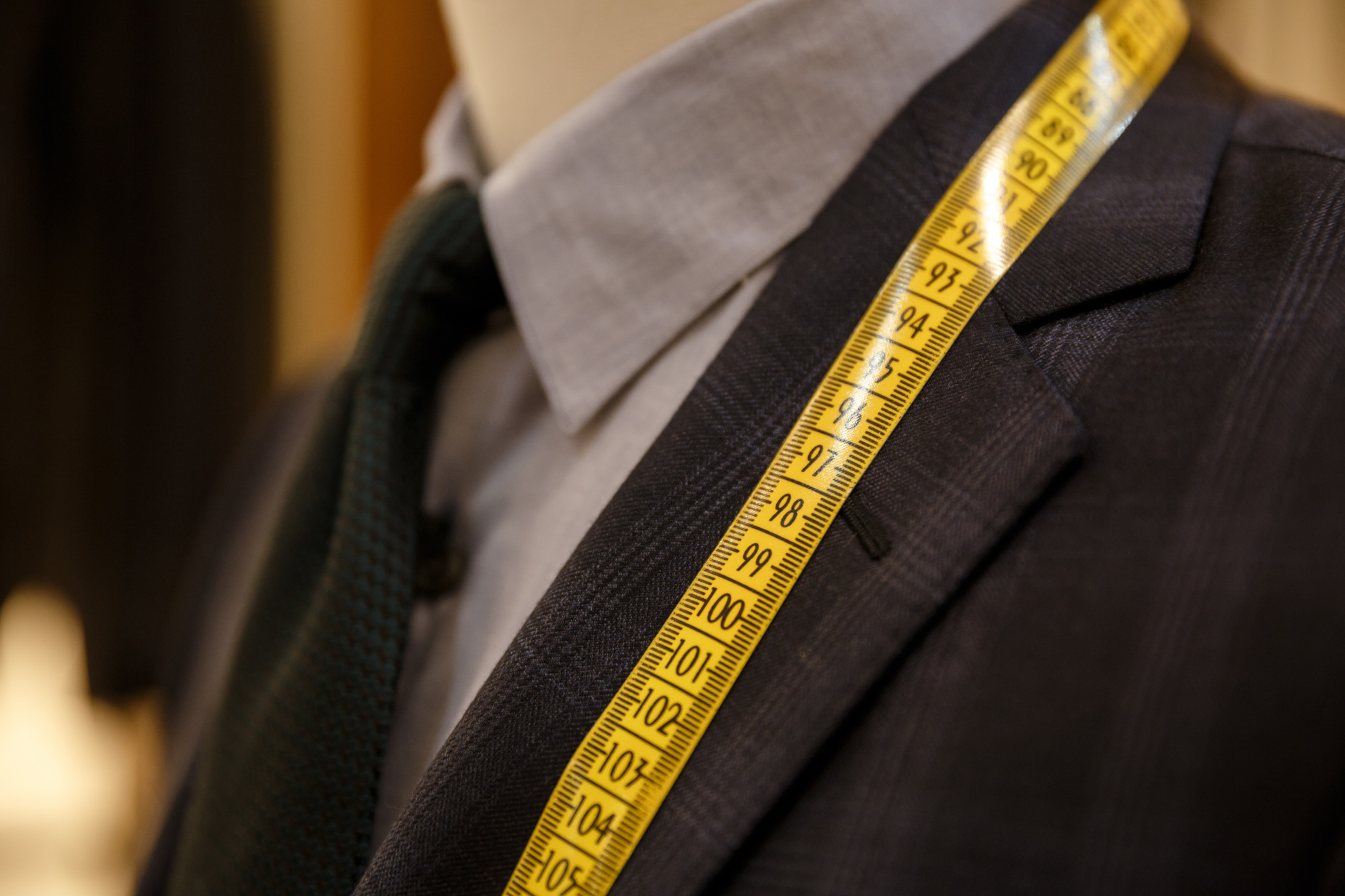 Close-up of a suit jacket on a mannequin with a yellow measuring tape draped over the shoulder.