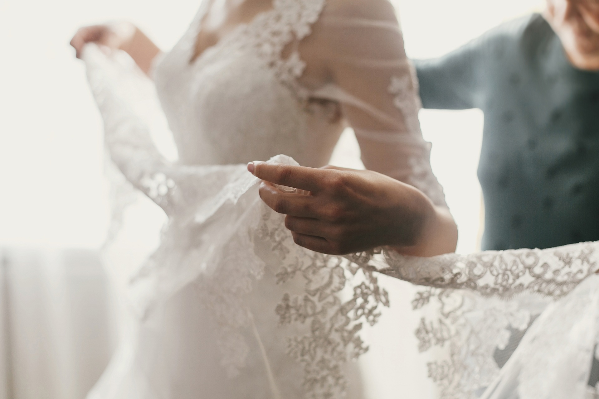 A bride in a lace wedding dress is having the fabric adjusted by another person, ensuring every detail is perfect before her Rancho Santa Margarita Wedding.