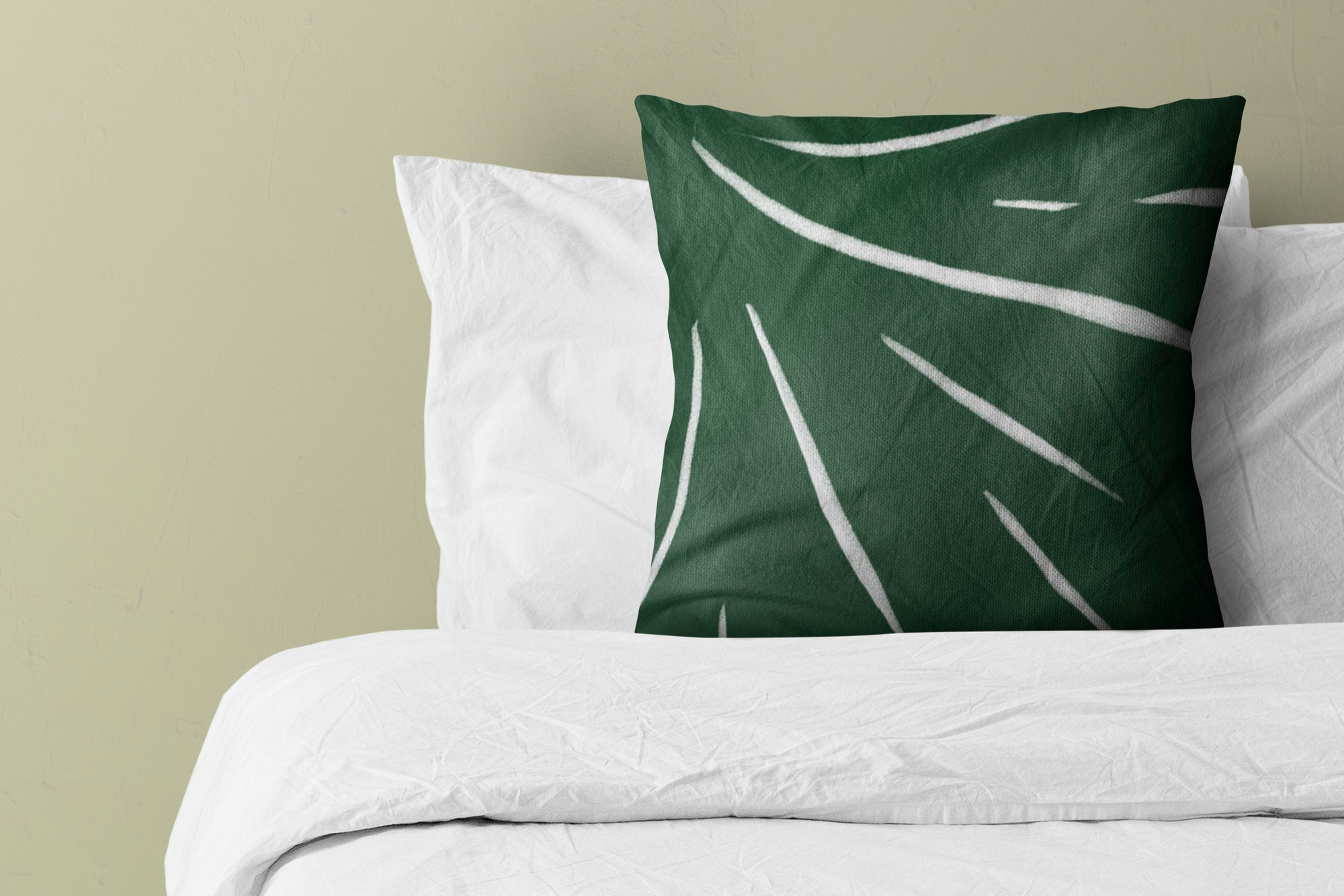 A white bed with a neatly arranged pillow featuring a dark green cover with white line patterns, set against a light green wall.