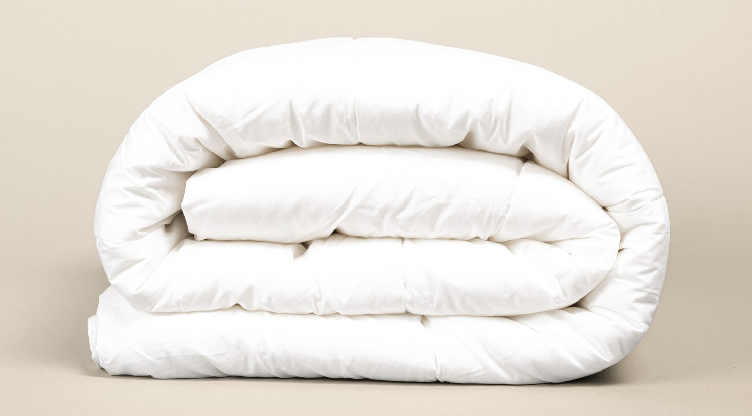 A neatly folded white comforter against a neutral background.