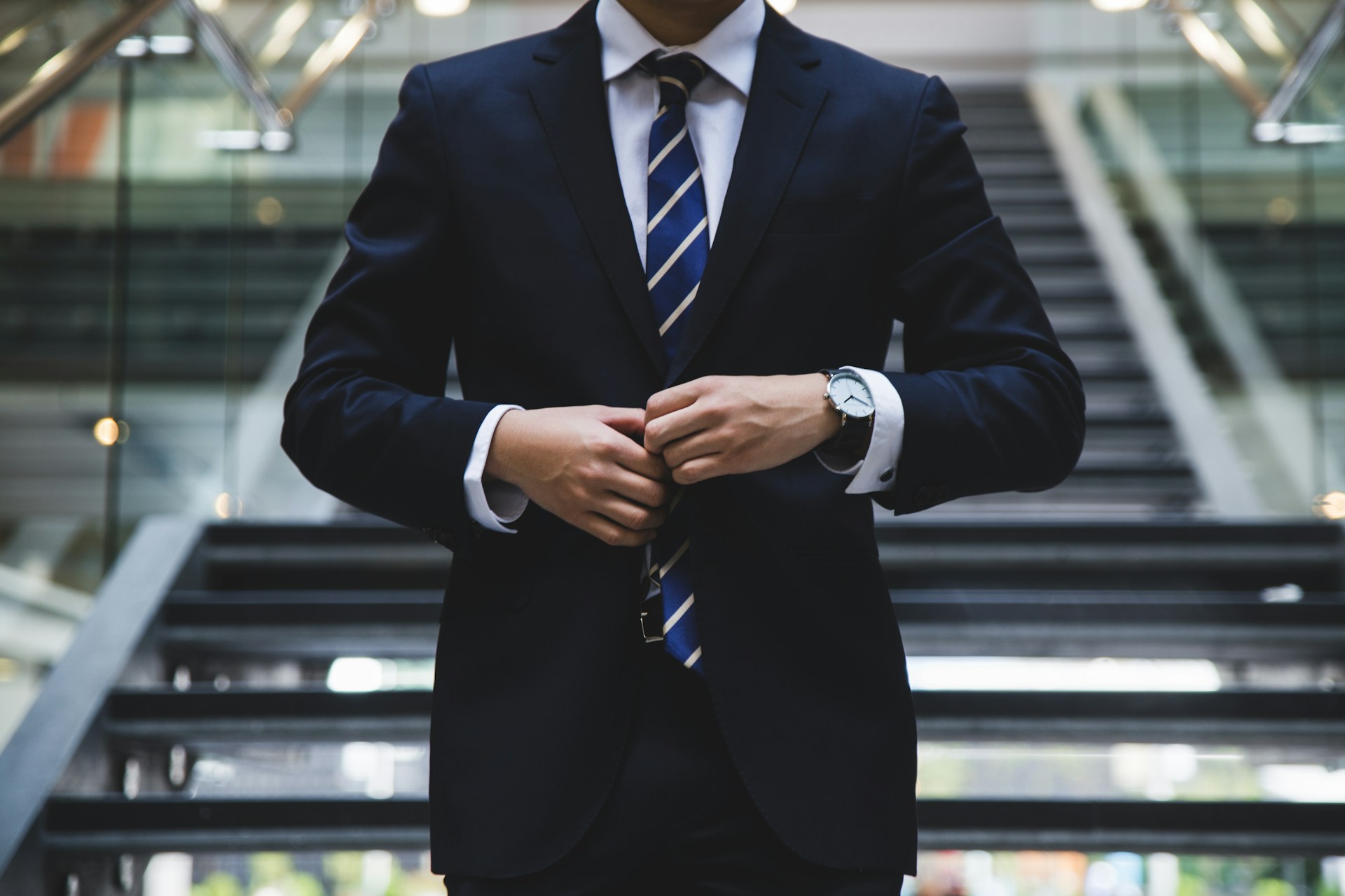 Person in a business suit adjusts their jacket in front of stairs.