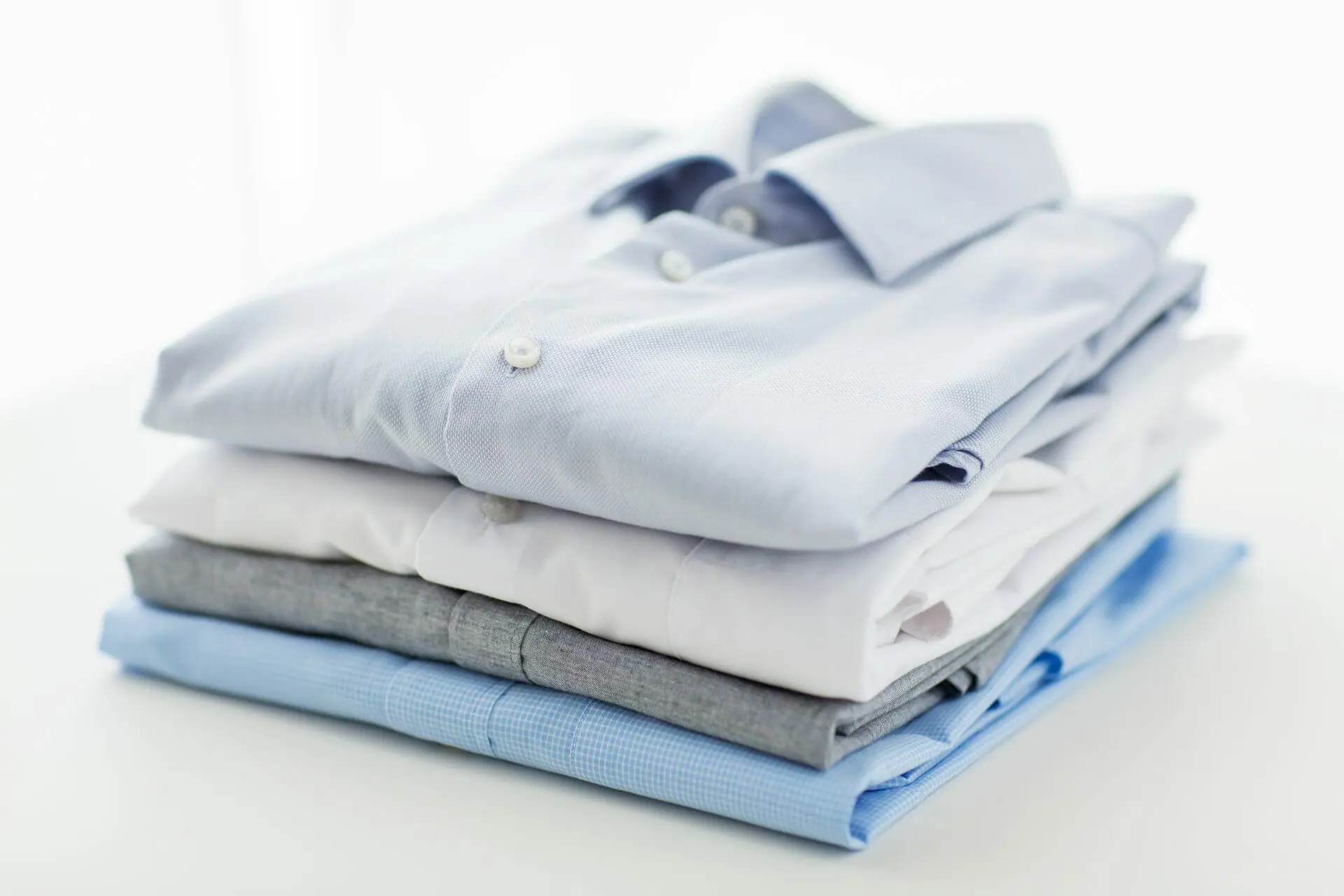 A neatly stacked pile of folded dress shirts in shades of blue, gray, and white.