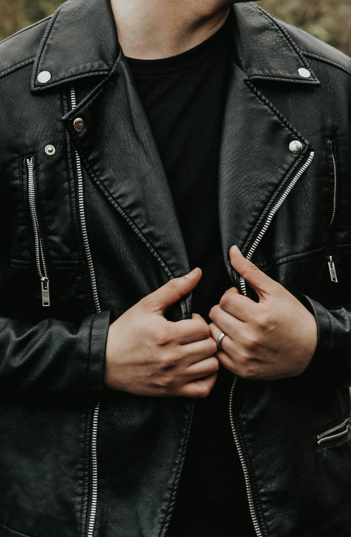Person wearing a black leather jacket and black shirt, holding the jacket's lapels with both hands.