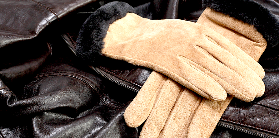 Tan suede gloves with black trim rest on a dark brown leather jacket.